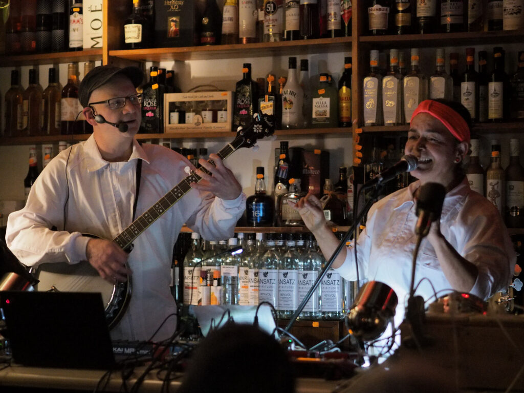 Oliver Stotz am Banjo blickt zu Sabine Marten, die gerade singt. Programm "Die Ex-Gewichtsheberin" in der Likörstube