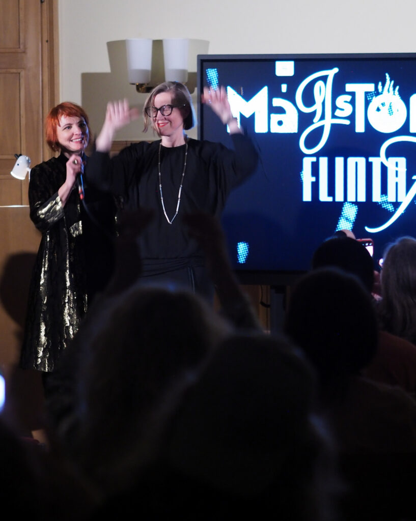 Moderatorin Anita Tokic neben Preisträgerin Nina Schedlmayer, die gerade ihren Preis, die goldene Nadel, erfreut hochhebt.